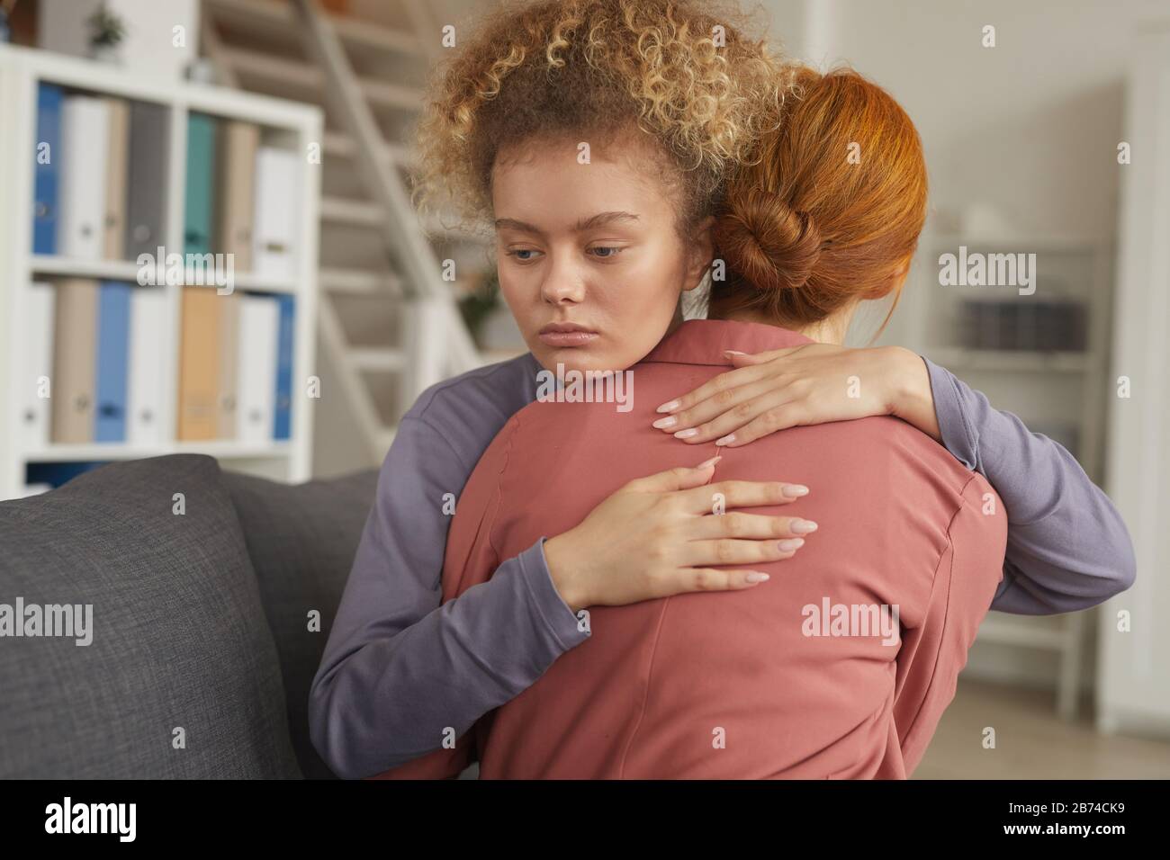 Junge Frau mit lockigen Haaren, die ihren Freund umarmte und unterstützte, während sie auf dem Sofa im Zimmer saß Stockfoto