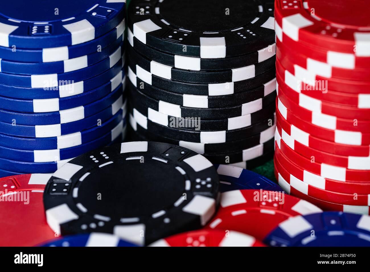 Ein Makrobild von Red Black und Blue Clay Poker Wettchips auf einer grünen Filzspielfläche. Lebendige Farben und schöner Kontrast. Es gibt ein einzelnes Stockfoto