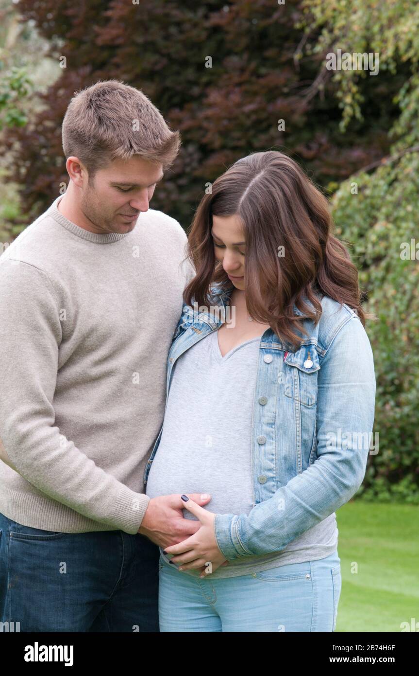 Schwangere junge Frau, die mit ihrem Partner steht und ihren Bauch zersäumt Stockfoto