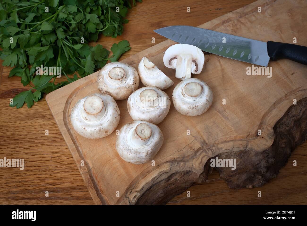 Gemeine weiße Pilze auf einem Hackbrett mit flacher beblätterter Petersilie Stockfoto