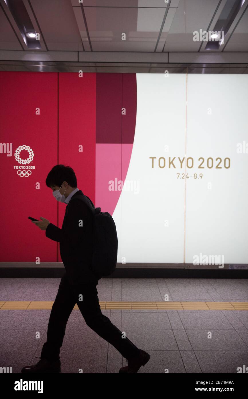 Ein Mann, der eine chirurgische Maske als präventive Maßnahme gegen das Corona-Virus trägt, läuft an einer Plakatwand in der Shinjuku-Station vorbei, die die Olympischen Spiele in Tokio 2020 fördert. Stockfoto