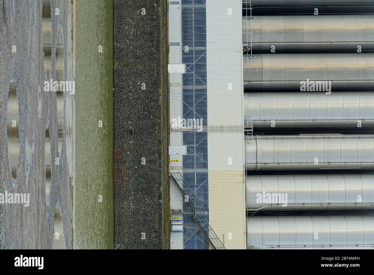 Vertikale Aufnahme von Metallsilos in einem Hafen mit Kai Fluss und eine Feldstraße runden die Szene ab Stockfoto