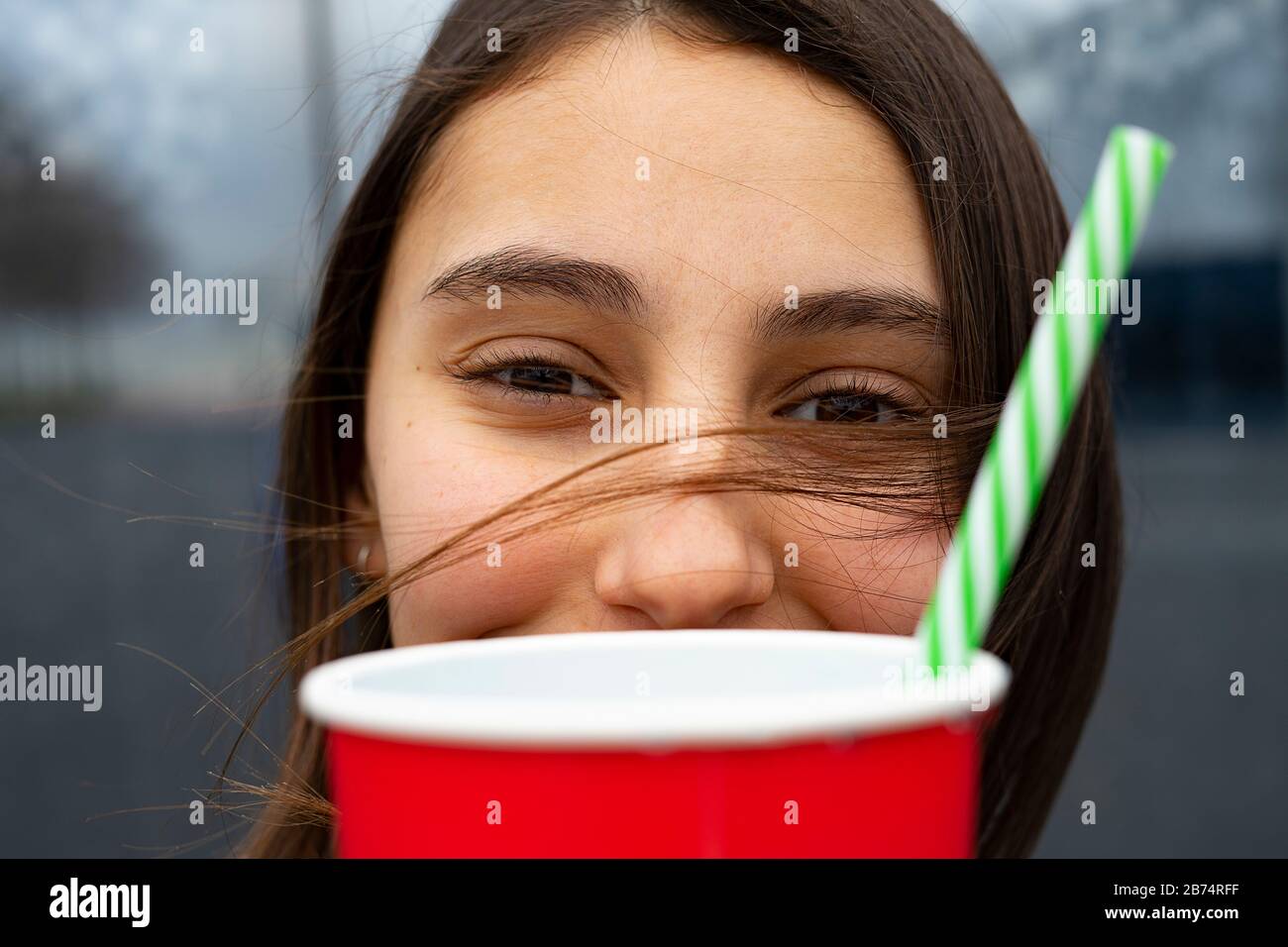 Frau mit ihren Haaren im Gesicht, die ein Glas mit einem bunten Strohhalm aufnimmt. Partykonzept. Stockfoto