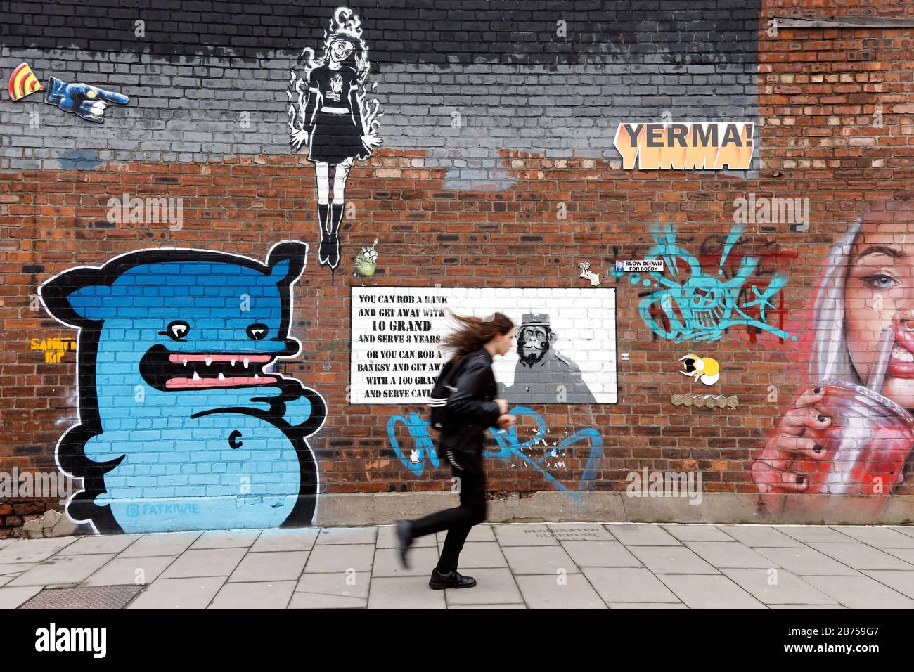 Eine Frau, die am 01.03.2019 an einer Hauswand mit Graffiti im Liverpooler Stadtteil Baltic Triangle vorbeijoggt. [Automatisierte Übersetzung] Stockfoto