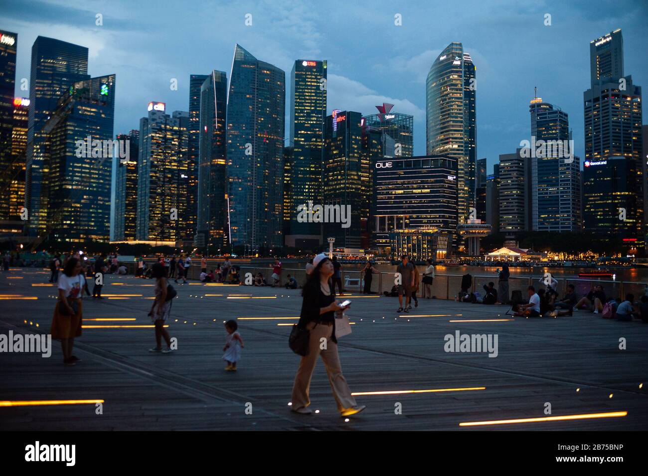 14.12.2018, Singapur, Republik Singapur, Asien - Menschen am Ufer des Singapur-Flusses in der Marina Bay mit der abendlichen Skyline des Geschäftsviertels im Hintergrund. [Automatisierte Übersetzung] Stockfoto