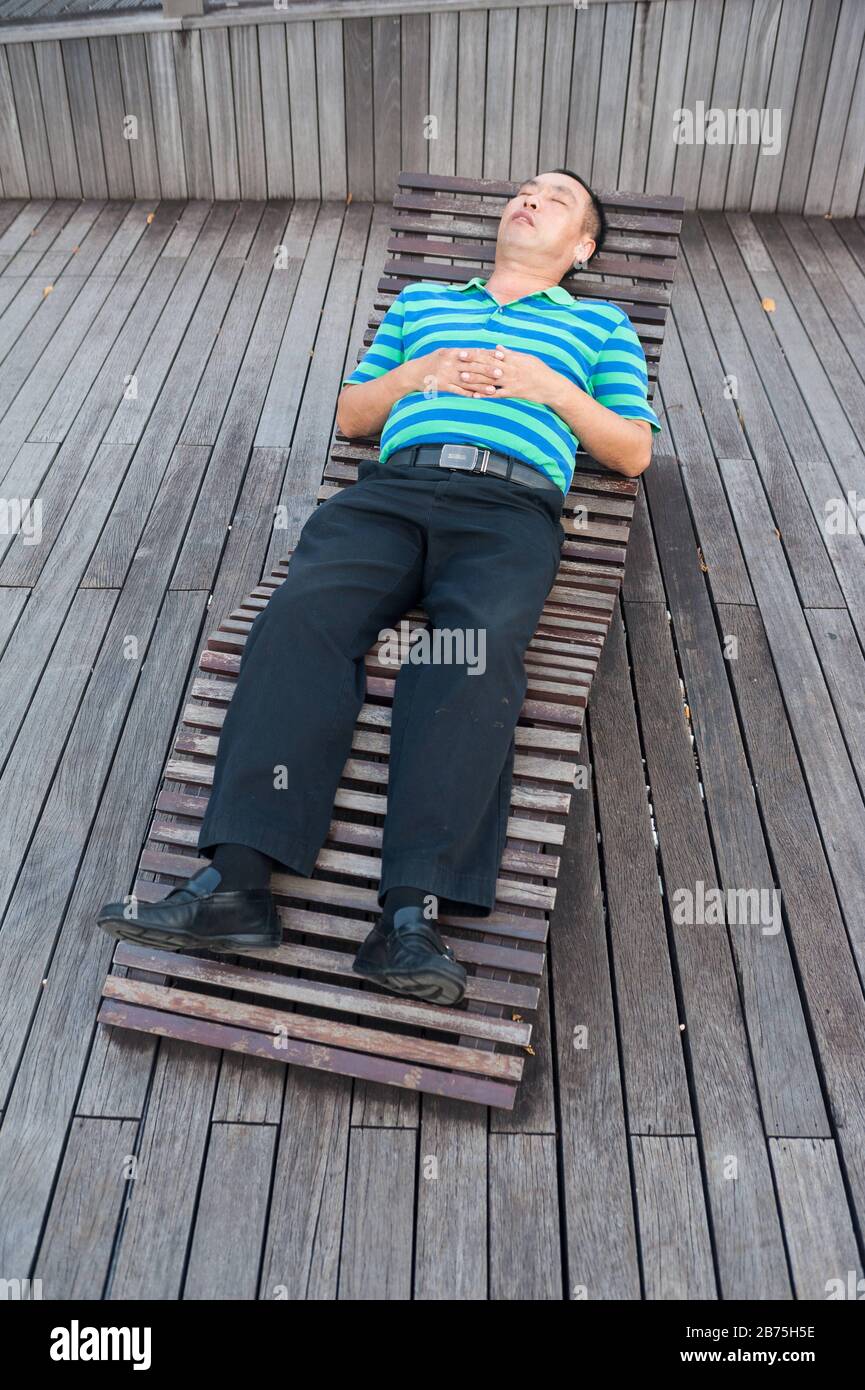 01.03.2018, Singapur, Republik Singapur, Asien - EIN Mann nimmt ein Nickerchen auf einer Holzkecke in der Marina Bay. [Automatisierte Übersetzung] Stockfoto