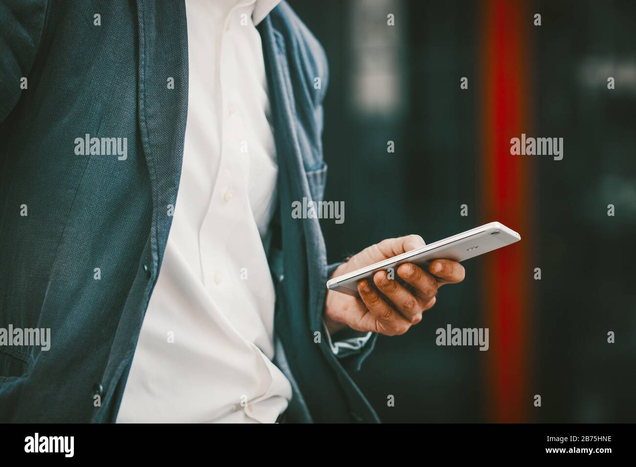 Mann in weißem Hemd und blauer Jacke außerhalb des Business Centers und SMS oder E-Mail am Telefon lesen. Nahaufnahme des Telefons in der Hand Stockfoto