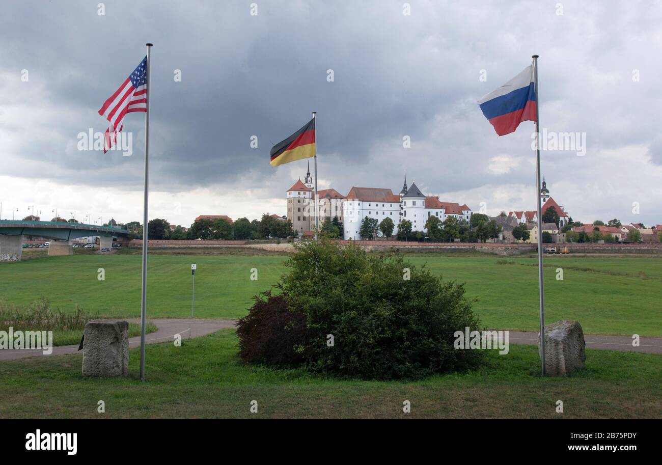 Eine amerikanische, russische und deutsche Flagge wird am 06.09.2017 in der Gedenkstätte "der Geist der Elbe" in Torgau fliegen. Die Gedenkstätte am Elbufer erinnert an die Begegnung zwischen Alliierten und sowjetischen Streitkräften im zweiten Weltkrieg Am 25. April 1945 fand hier der "Handschlag von Torgau" mit amerikanischen und russischen Soldaten statt. Schloss Hartenfels im Hintergrund. [Automatisierte Übersetzung] Stockfoto