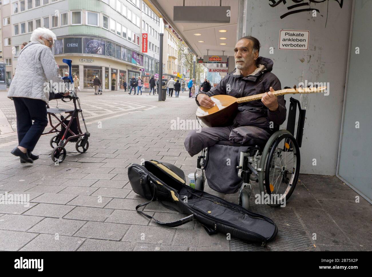 Ein türkischer Mann im Rollstuhl spielt am 21.04.2017 türkische Musik an der Bahnhofstraße in Gelsenkirchen, während eine alte Frau in einem Wanderer vorbeiläuft. Mit einer Arbeitslosenquote von 14 Prozent, Januar 2017, und einem Ausländeranteil von knapp 20 Prozent, steht die Stadt Gelsenkirchen vor großen sozialen Problemen. [Automatisierte Übersetzung] Stockfoto