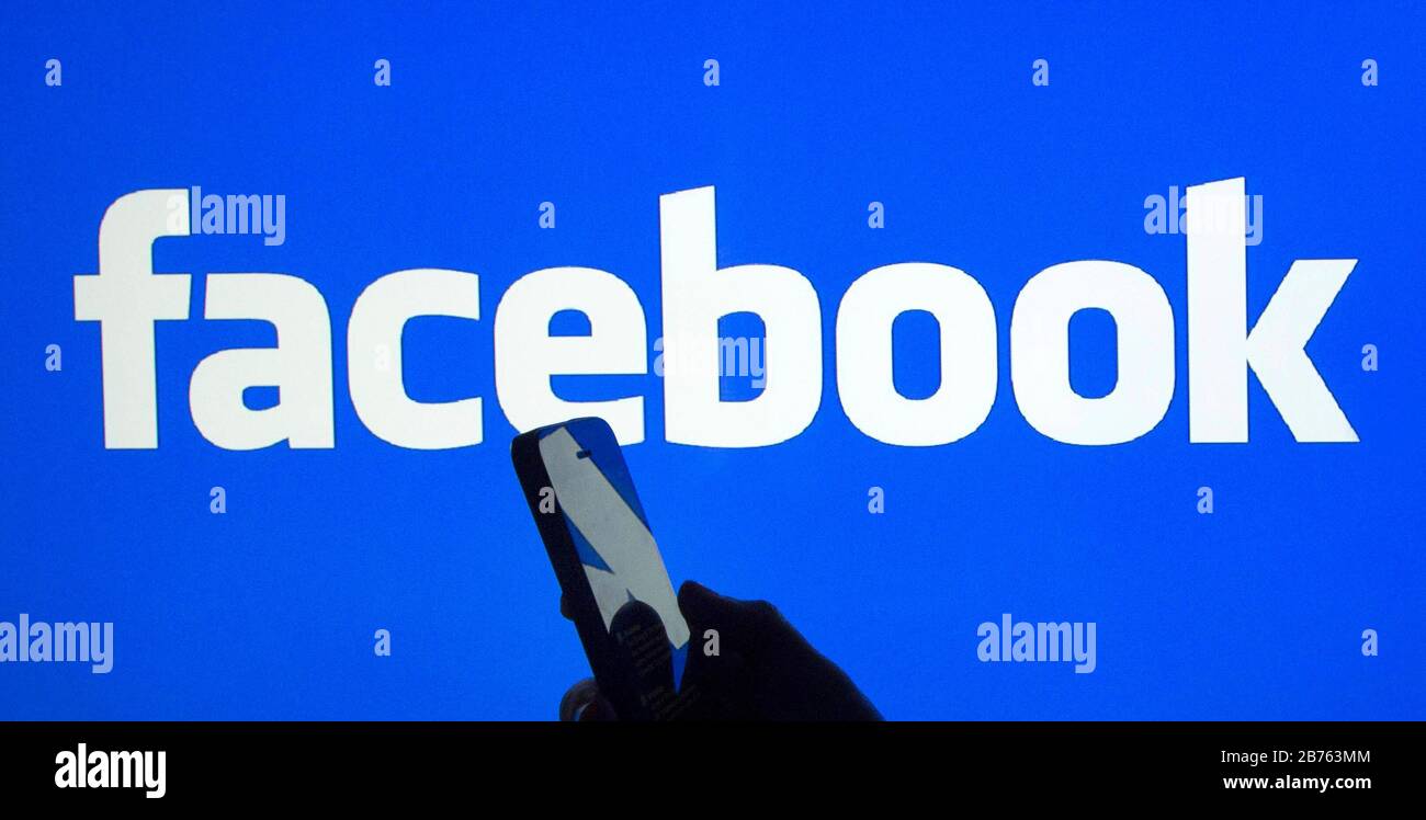 Die Silhouette einer Hand mit einem Smartphone in der Hand ist vor einem Facebook-Logo zu sehen, am 23.03.2016 [automatisierte Übersetzung] Stockfoto