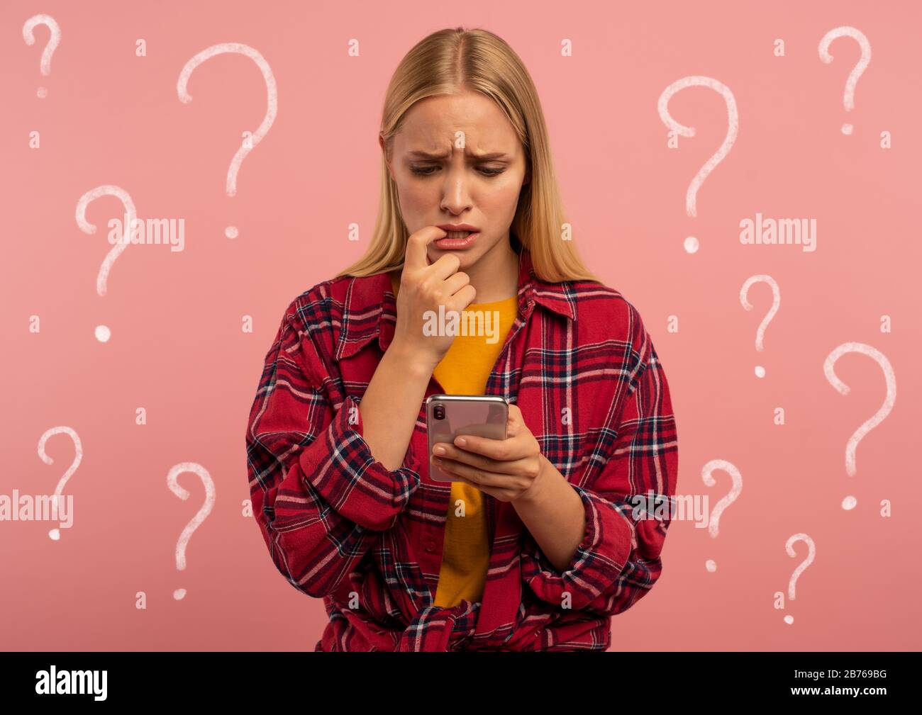 Mädchen mit ihrem Smartphone. Erschrocken und ängstlich Ausdruck. Rosafarbener Hintergrund Stockfoto