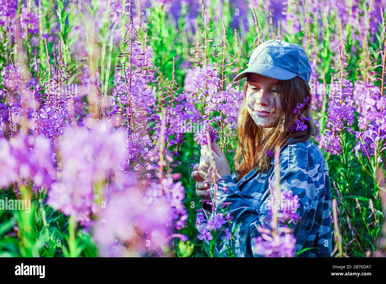 Ein junges Mädchen in Tarnung im hohen Gras mit Blumen Stockfoto