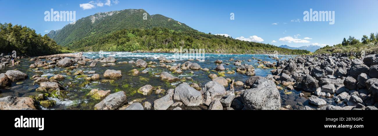 Panoramalandschaft des Flusses Petrohue voller großer Steine mit einer bewaldeten kleinen Bergkette Stockfoto