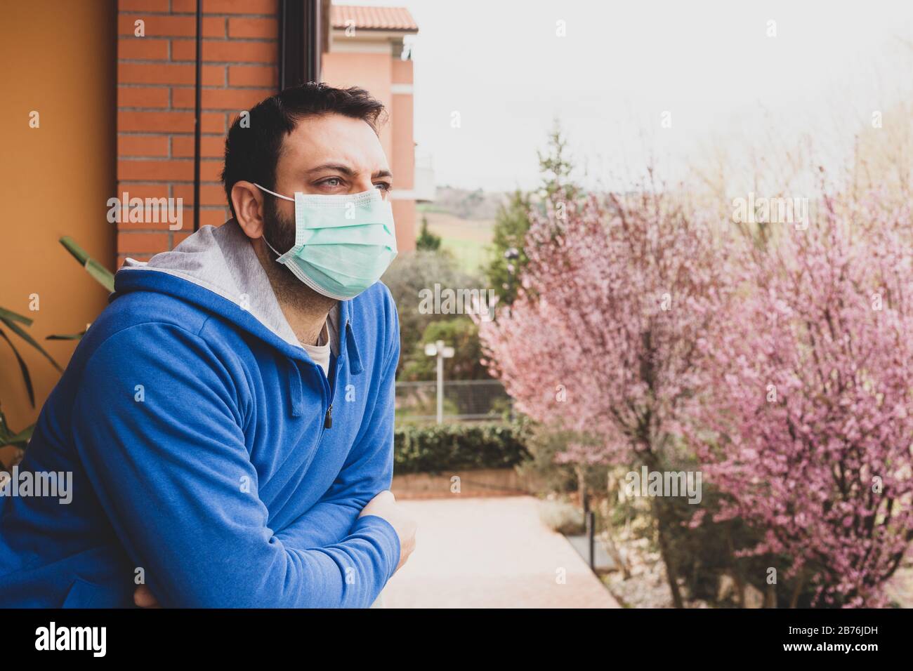 Junger kaukasischer Mann mit Maske, der während der Quarantäne auf die Heimatterrasse blickt, da Coronavirus kovid19 pandemic ist. Stockfoto