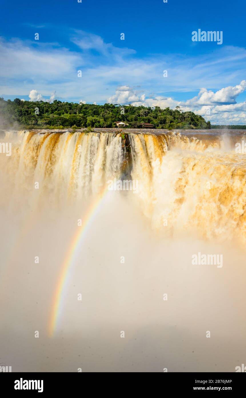 Blick auf einen Teil des Garganta del Diablo im Nationalpark Iguazú mit Regenbogen und einen Teil der brasilianischen Seite des Parks mit vielen Bäumen Stockfoto