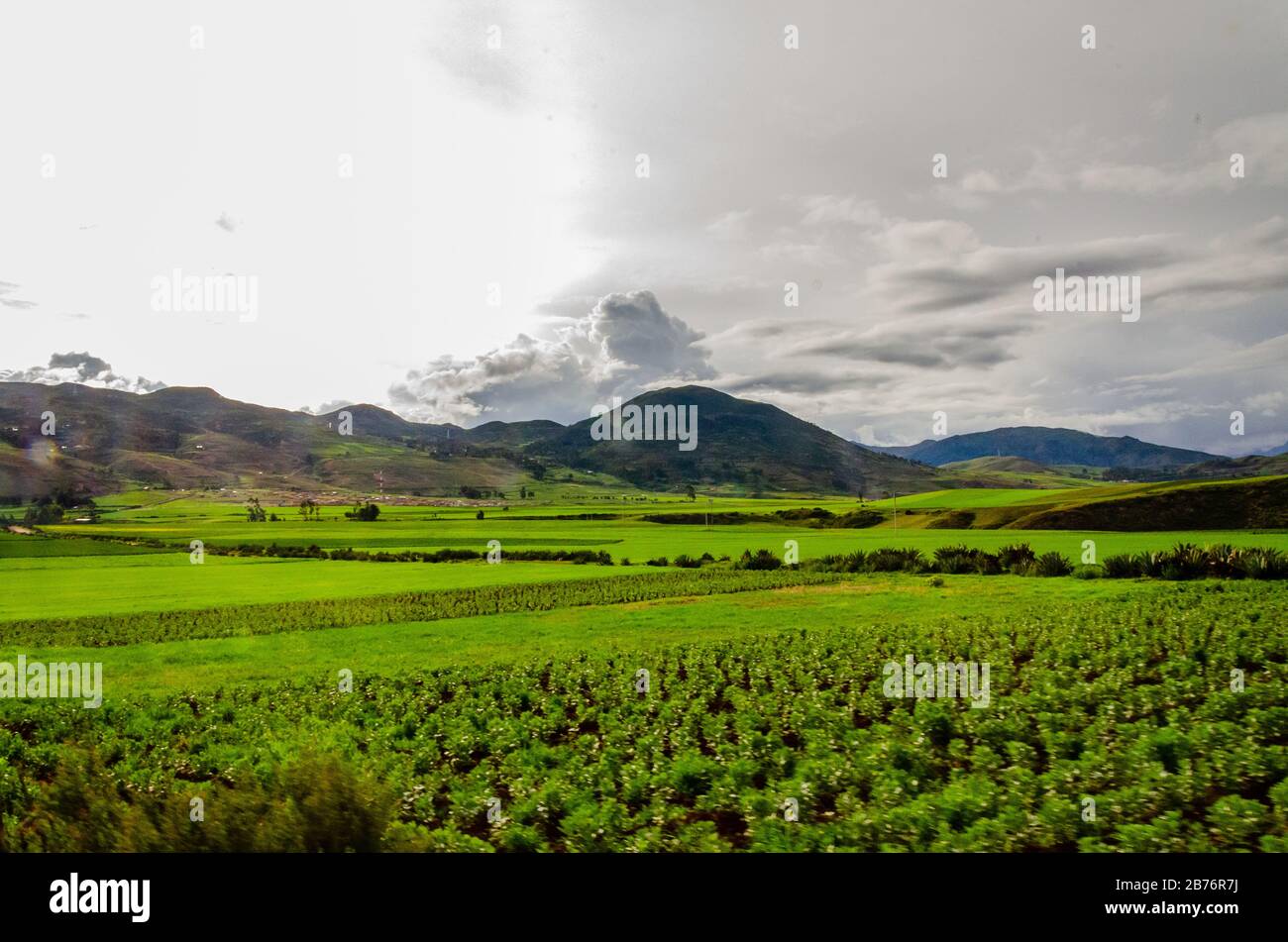 Grüne Felder mit Wolken und Bergen auf der Straße nach Moray, Peru Stockfoto