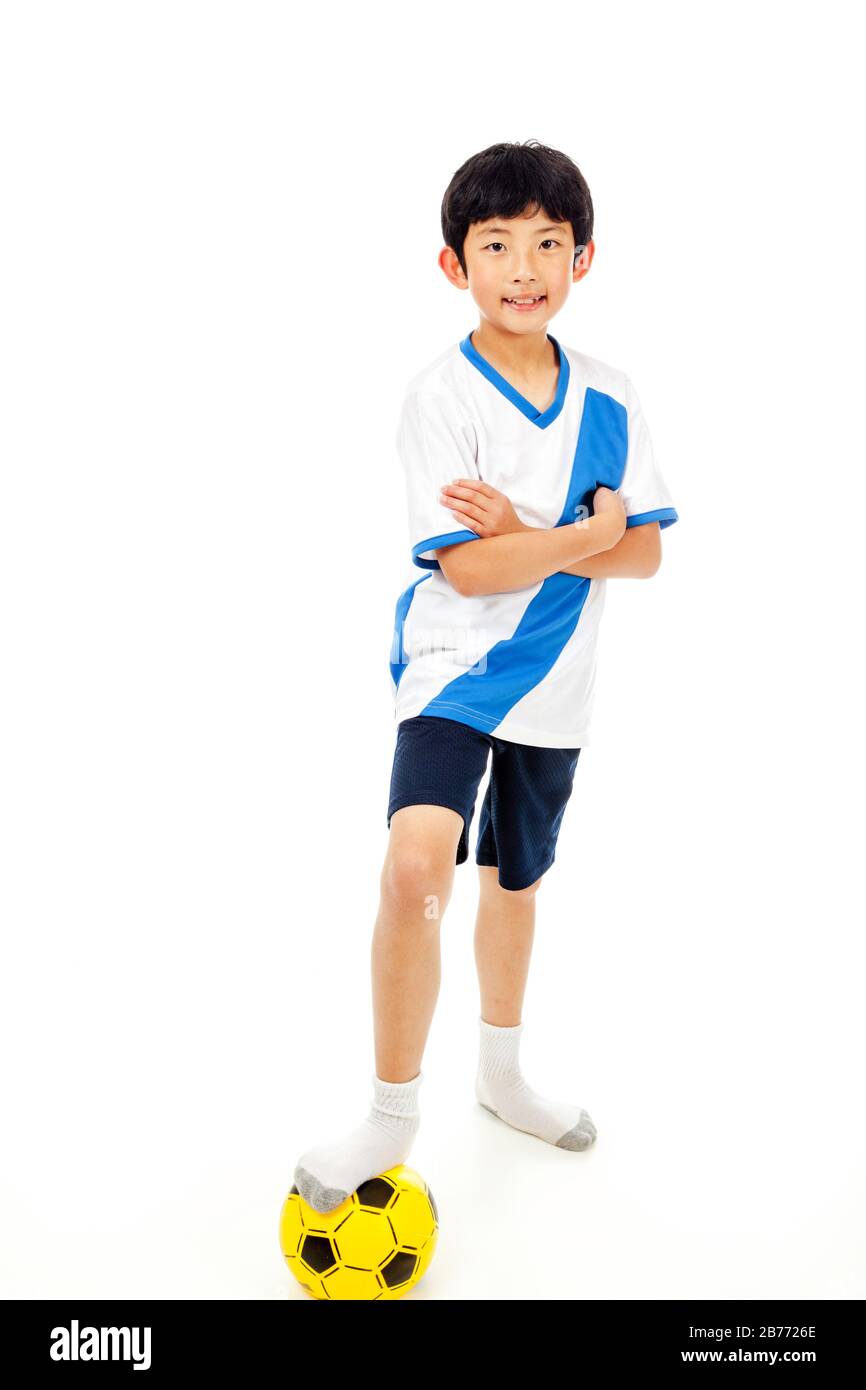 Fröhlicher junger asiatischer Junge mit Fuß auf Fußball isoliert auf weißem Hintergrund. Stockfoto