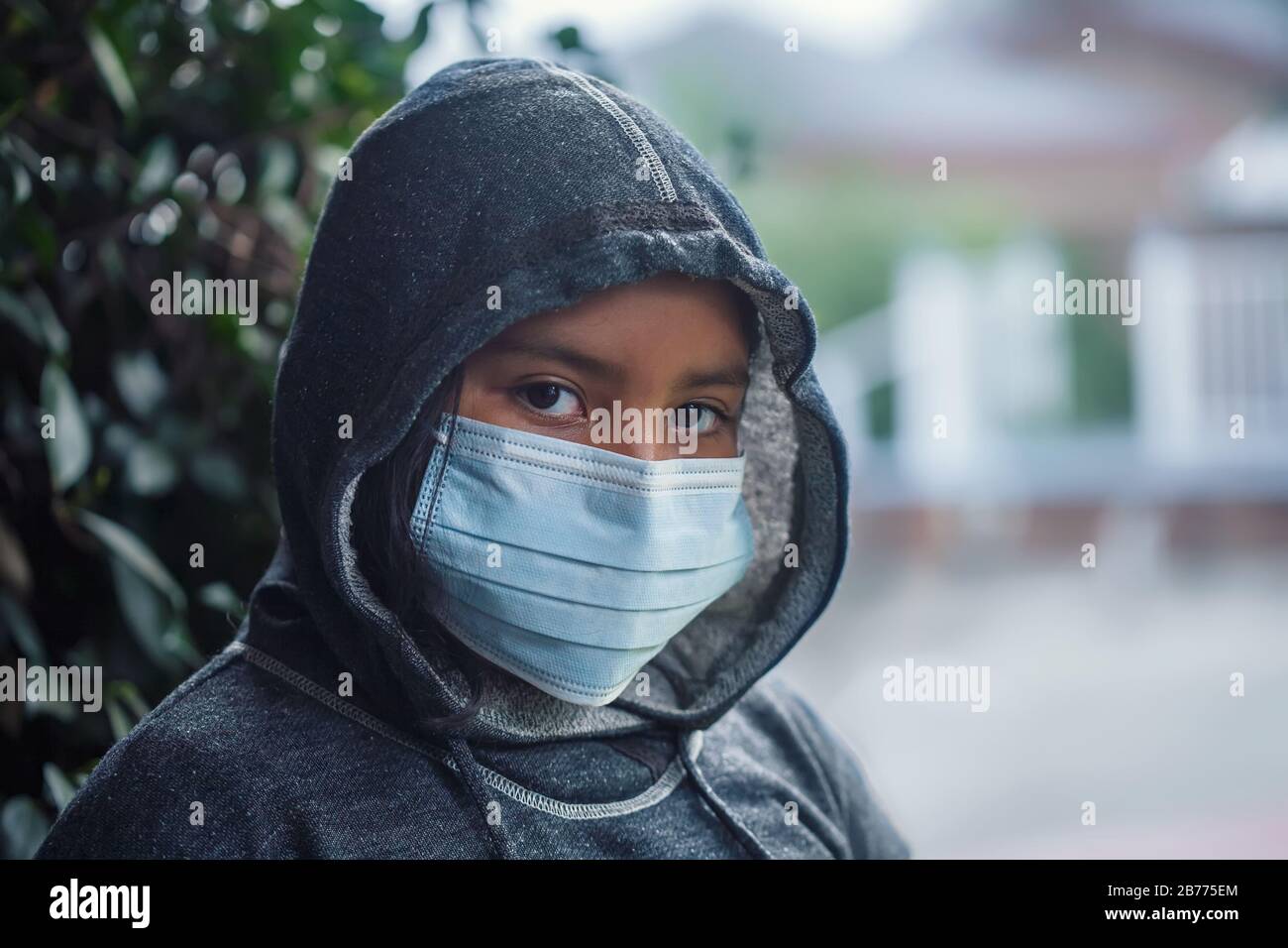 Latino 9-jähriges Mädchen oder Student, das ein Sweatshirt mit Kapuze und eine medizinische Gesichtsmaske trägt, um die Ausbreitung von Infektionskrankheiten zu verhindern. Stockfoto