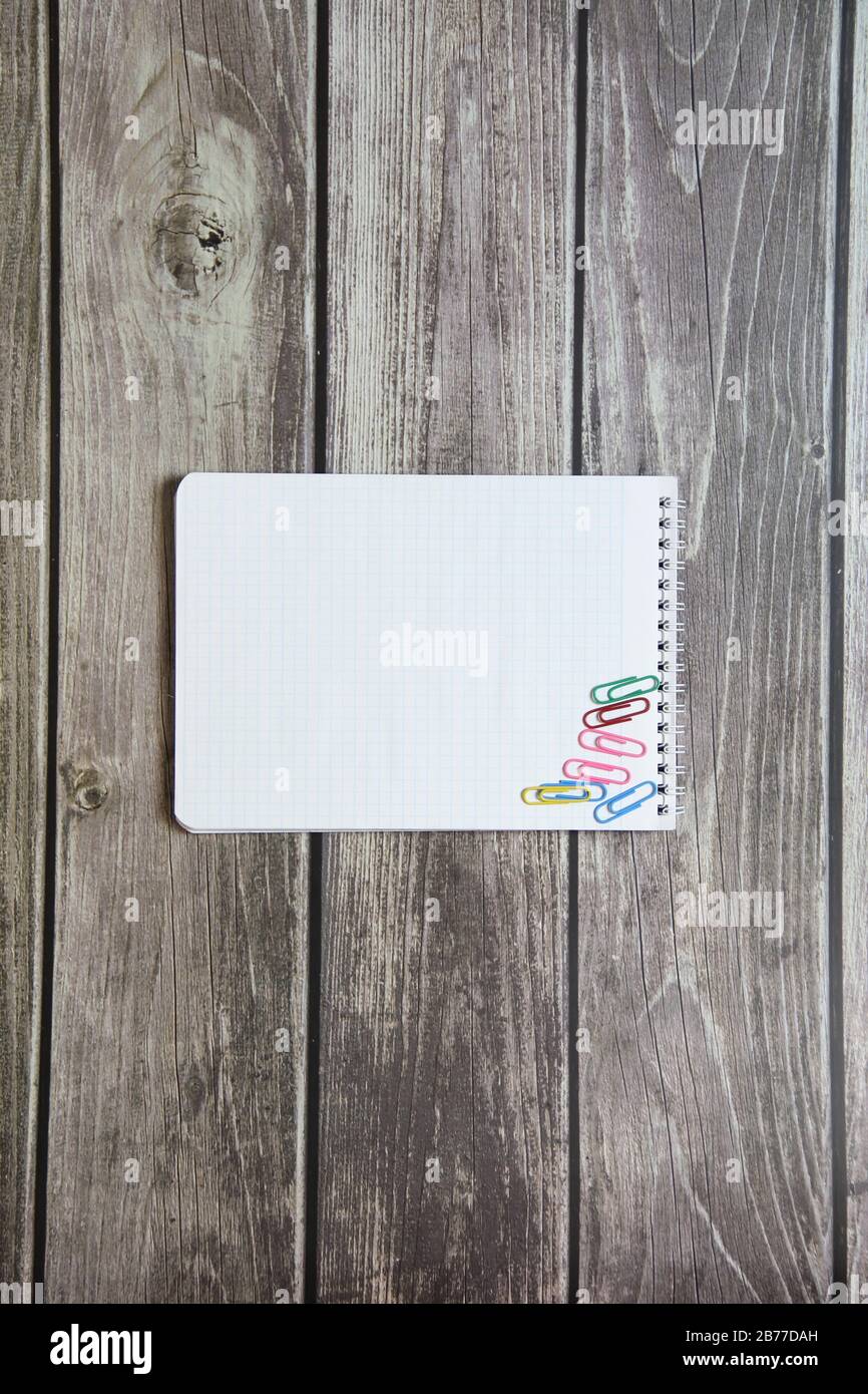 Notepad mit einem leeren weißen Blatt in einem Schachpapier mit Büroklammern liegt auf dem Hintergrund von Holzbrettern Stockfoto