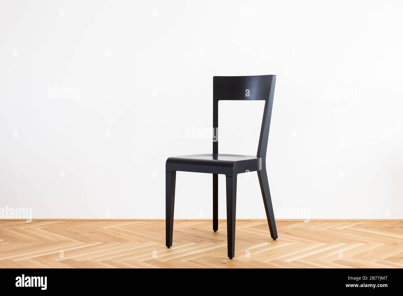 Moderner, vereinfachter schwarzer Stuhl auf einem Holzflor vor weißem Hintergrund Stockfoto