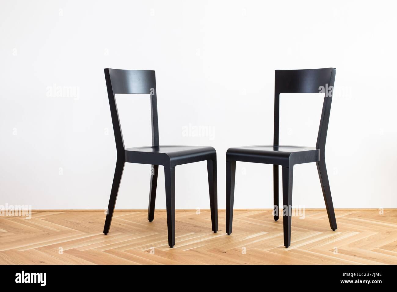 Moderne, stark vereinfachte schwarze Stühle auf einem Holzflor vor weißem Hintergrund Stockfoto
