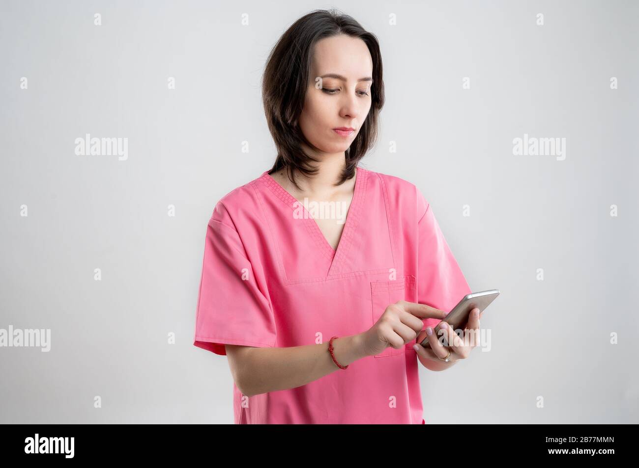 Junge Frau medizinische Fachkrankenschwester oder Arzt mit pinkfarbenen Krankenhauskleidung, mit braunen Haaren, Smartphone halten, SMS senden, Nachrichten senden po Stockfoto