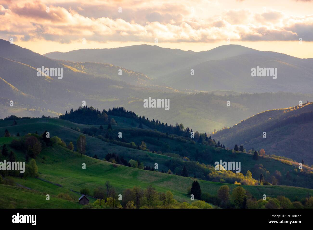 Bergiges ländliches Gebiet. Landwirtschaftliche Felder auf Hügeln mit Wald. Schöne und lebendige Landschaft mit bewölktem Himmel bei Sonnenuntergang Stockfoto