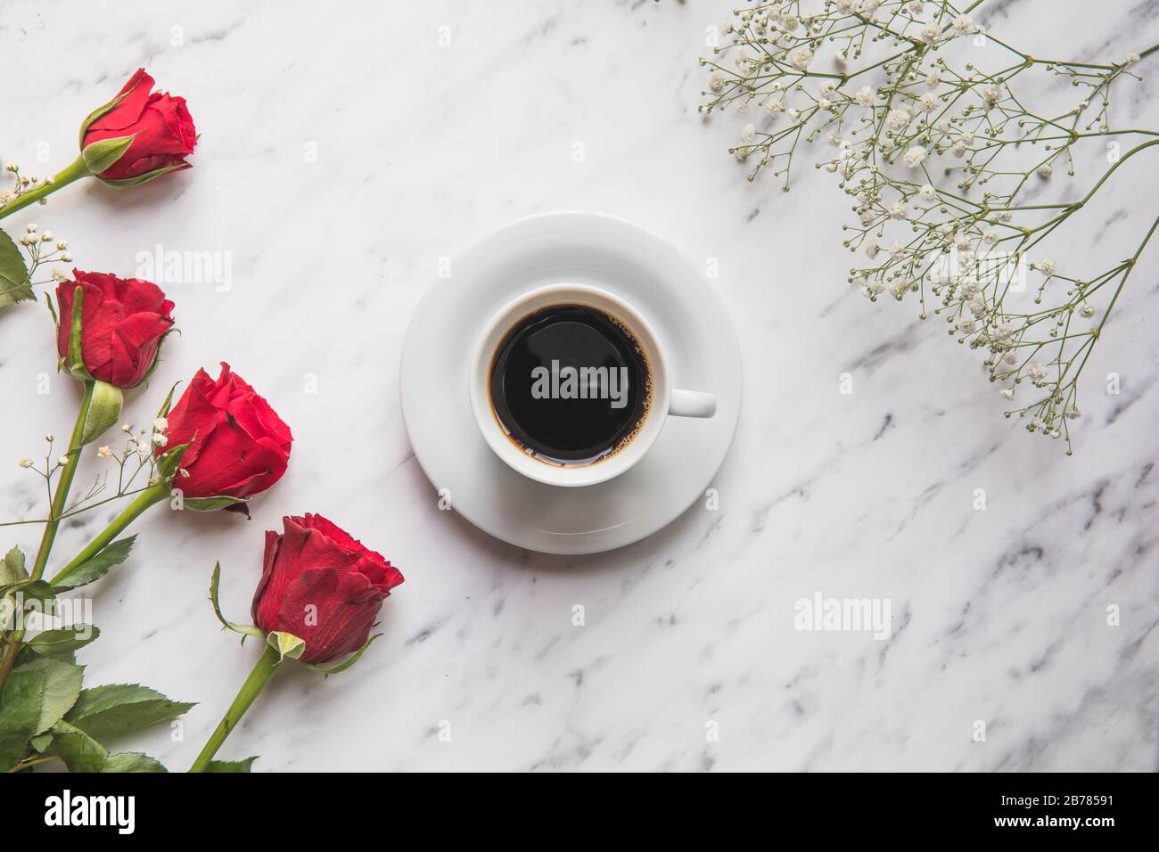 Eine Tasse schwarzen Kaffee, rote Rosen und Gypsophila Blumen auf einem Marmortisch. Flaches Lay von oben gesehen. Stockfoto