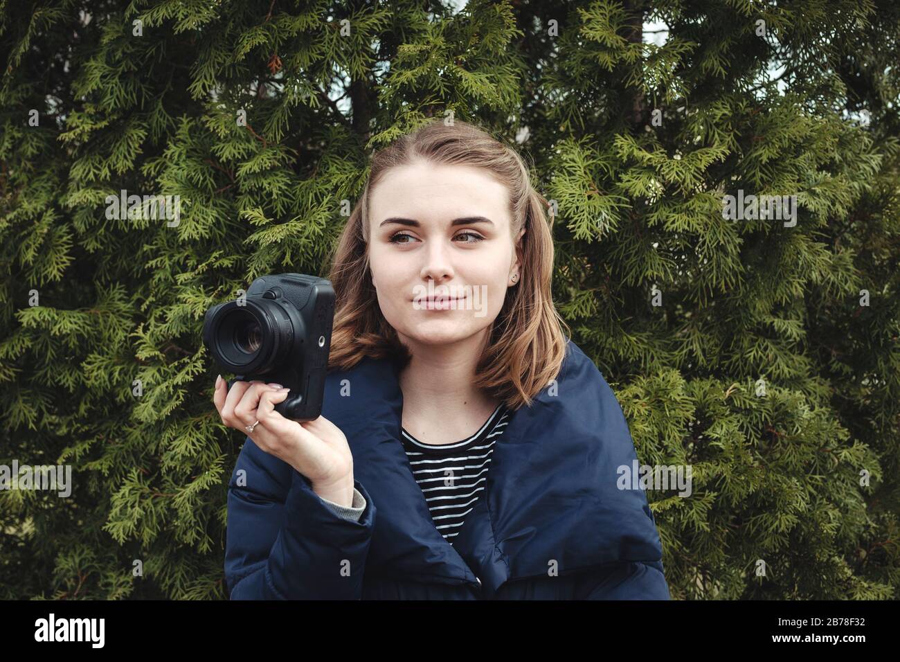 Attraktive lächelnde Fotografin hält ihre Kamera in einer Hand Stockfoto