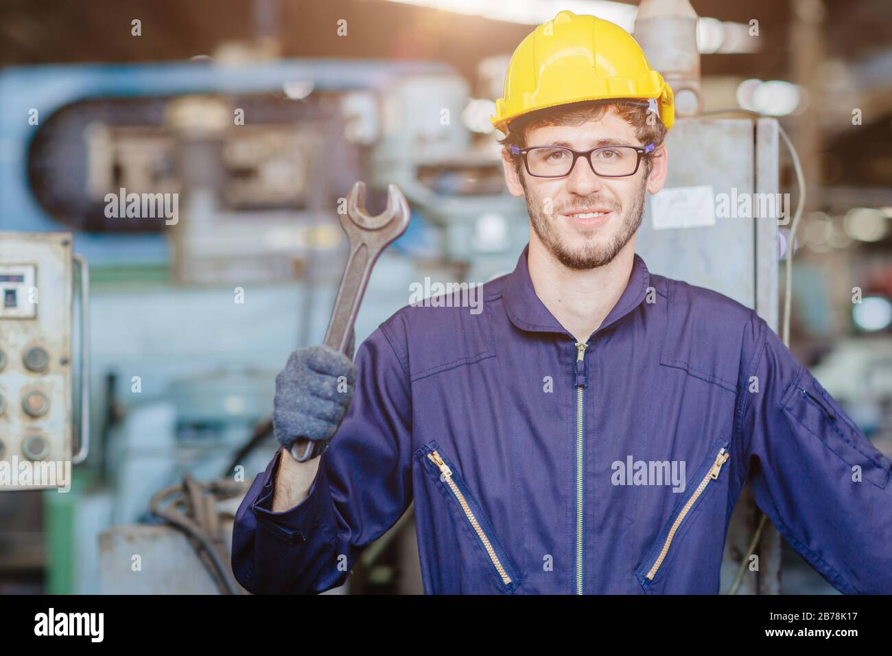 Glücklicher amerikanischer Teen Worker Handle Wrench.Engineer lächelt für Service Maintenance FIX Maschine in schwerer Industrie mit Safty Anzug und Helm. Stockfoto