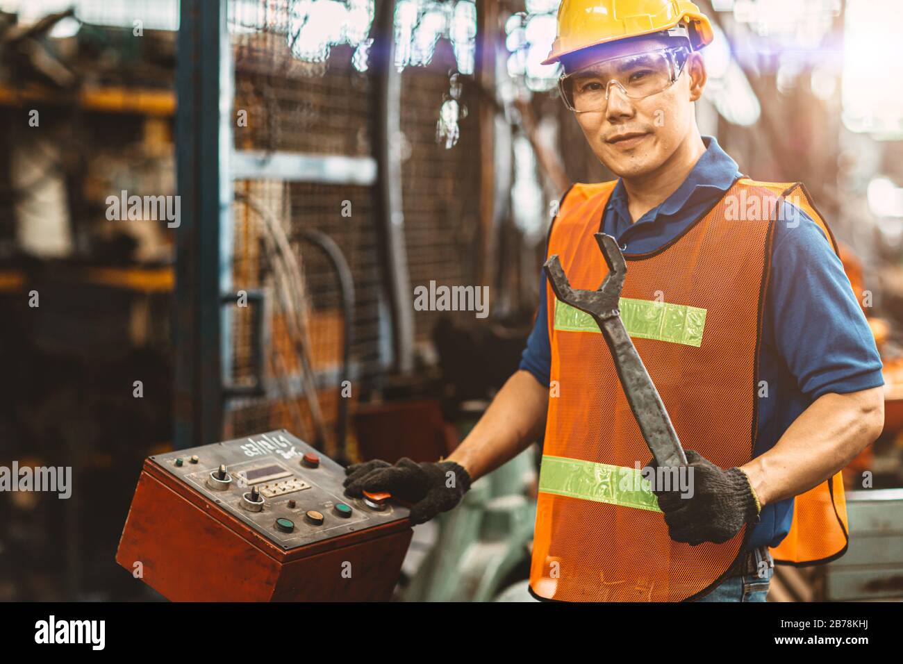 Portrait asiatisch-thailändischstämmiger Arbeiter fröhliche lächelnde Arbeiter, die in einer schweren Industriefabrik arbeiten, um die Maschine mit einem großen Schraubenschlüssel zu fixieren. Stockfoto