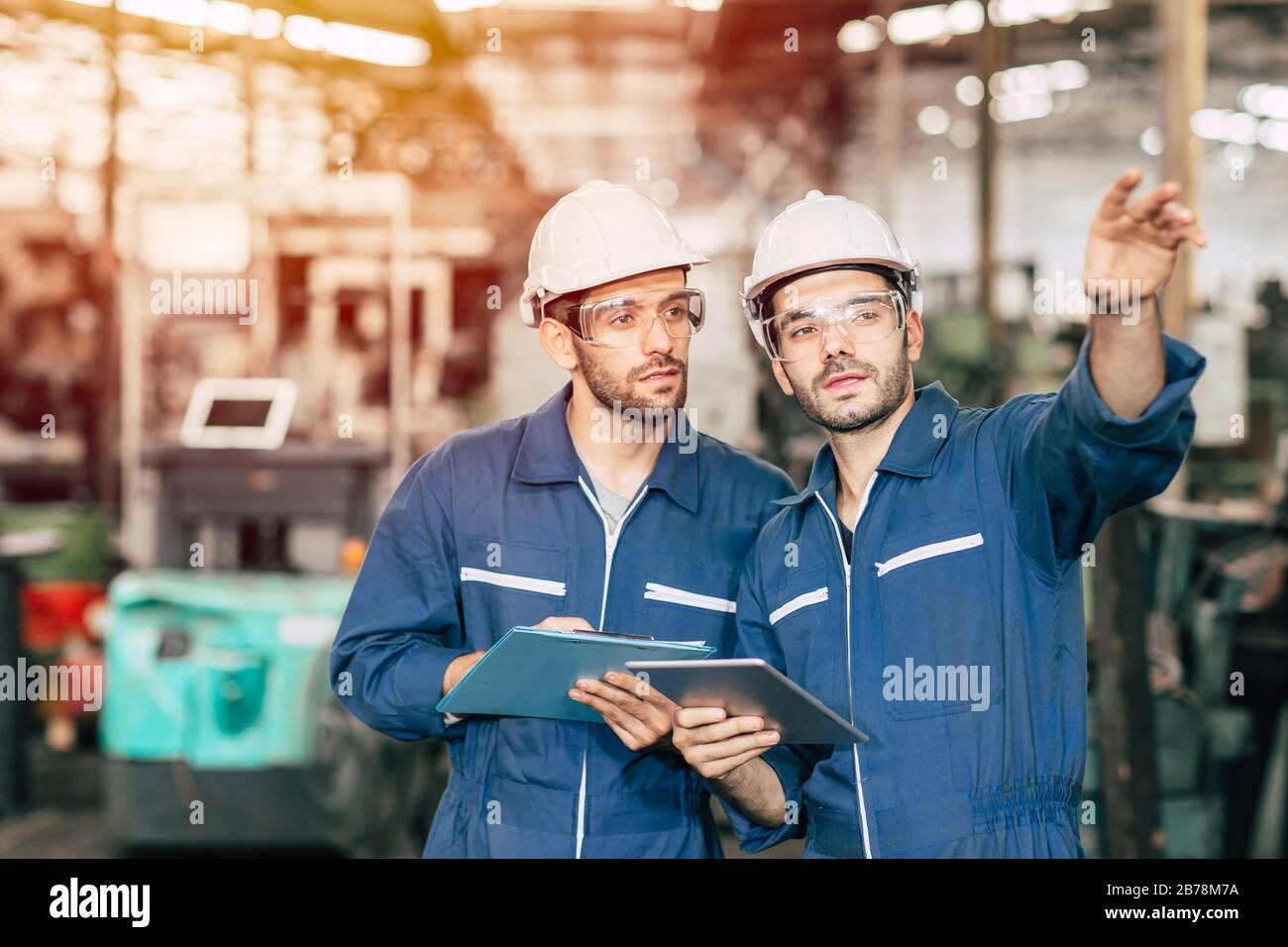 Zwei Techniker arbeiten zusammen mit Sicherheitsuniform und weißem Helm, um in der Industrie zu arbeiten, die Werkstafel zu handhaben. Stockfoto