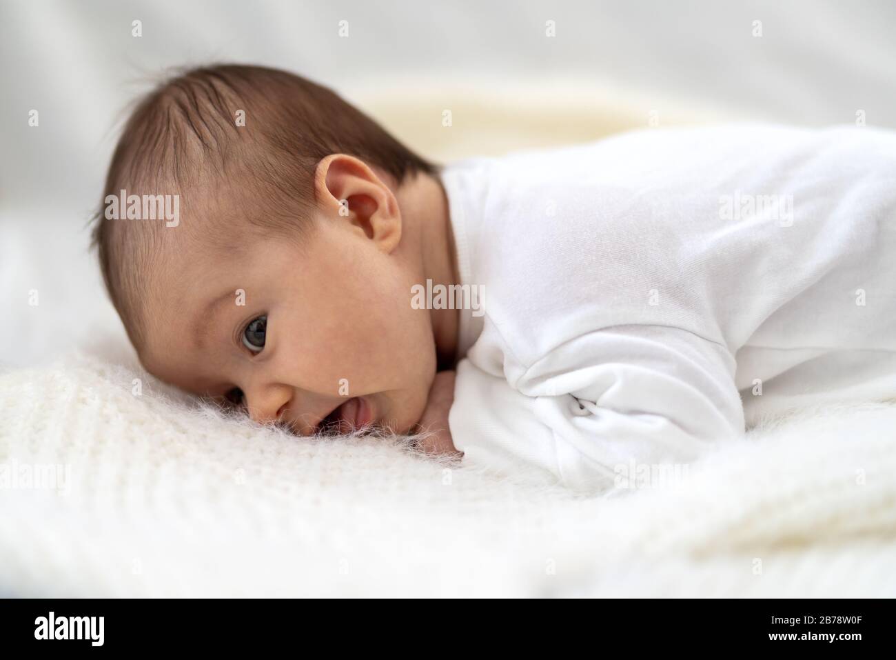 Ein 3-wöchiges altes kaukasisches Baby lächelt, während er sich auf ein flauschiges Daunenbett auf ein Bett legt Stockfoto