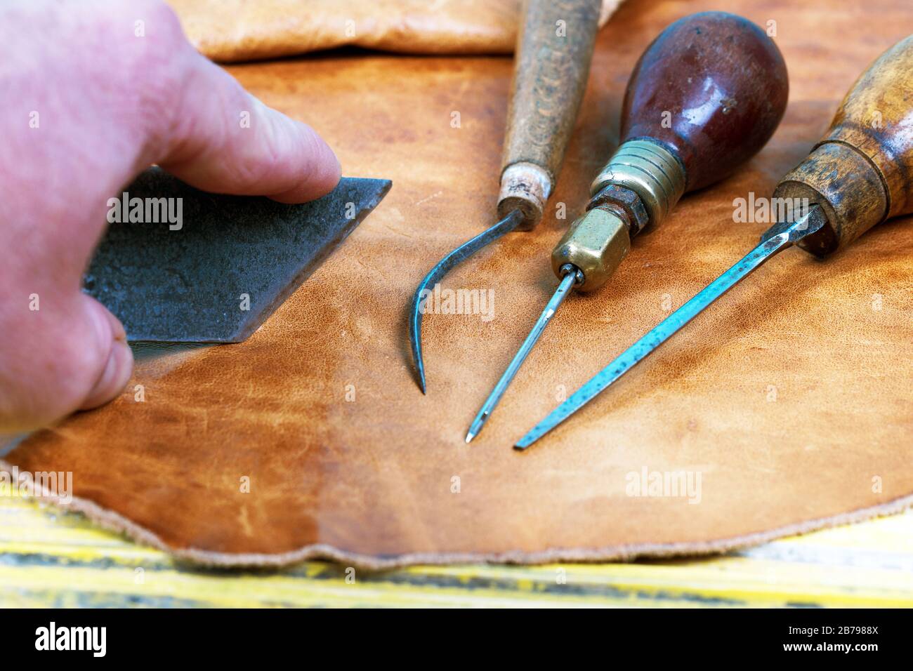 Handwerkzeuge aus Leder auf Holzhintergrund. Schreibtisch mit Lederhandwerk. Ein Teil der handgefertigten Werkzeuge auf einem Arbeitstisch Stockfoto
