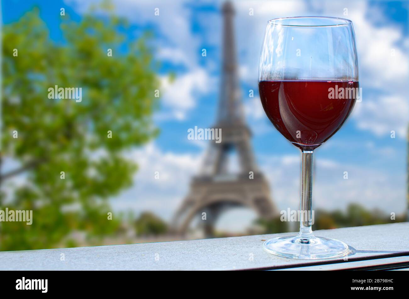 Glas Wein auf dem Eiffelturm verwischt den Hintergrund. Sonniger Blick auf das Glas Rotwein mit Blick auf den Eiffelturm in Paris, Frankreich Stockfoto