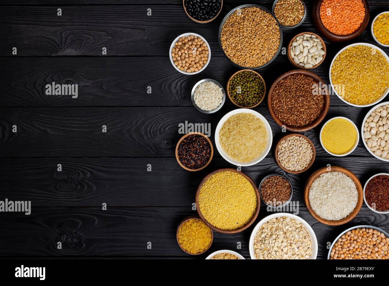 Verschiedene Getreide, Körner, Samen, Grütze, Hülsenfrüchte und Bohnen in Schalen auf schwarzem Holz- Hintergrund mit Kopie Raum Stockfoto