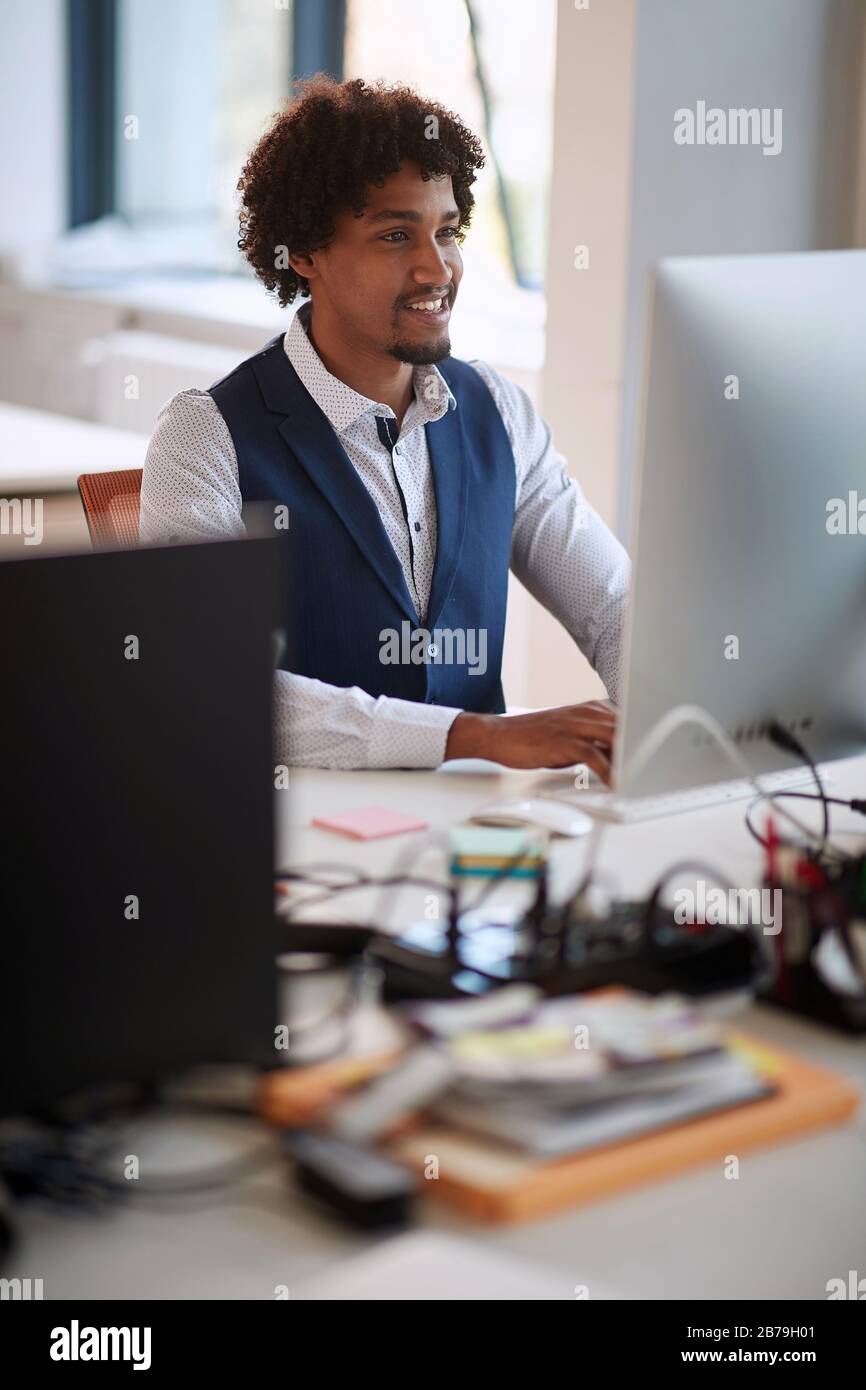 Erfolgreicher junger afroamerikanischer Geschäftsmann, der an Computer arbeitet. Modernes High-Tech-Büro. Stockfoto