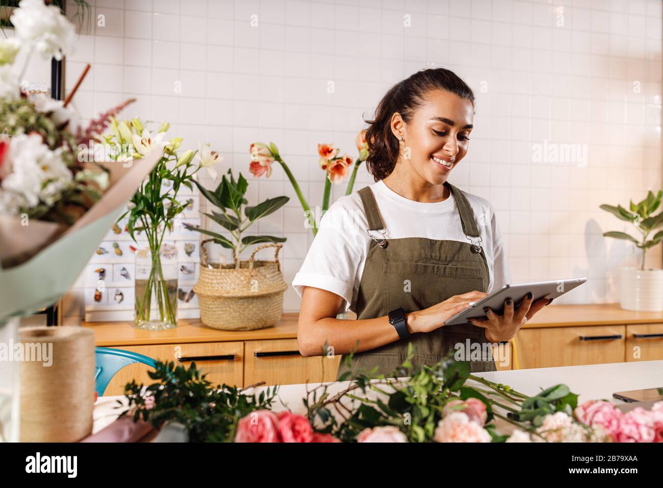 Junge Floristin macht sich Notizen auf einer digitalen Tablette. Frau überprüft Online-Bestellungen im Shop. Stockfoto