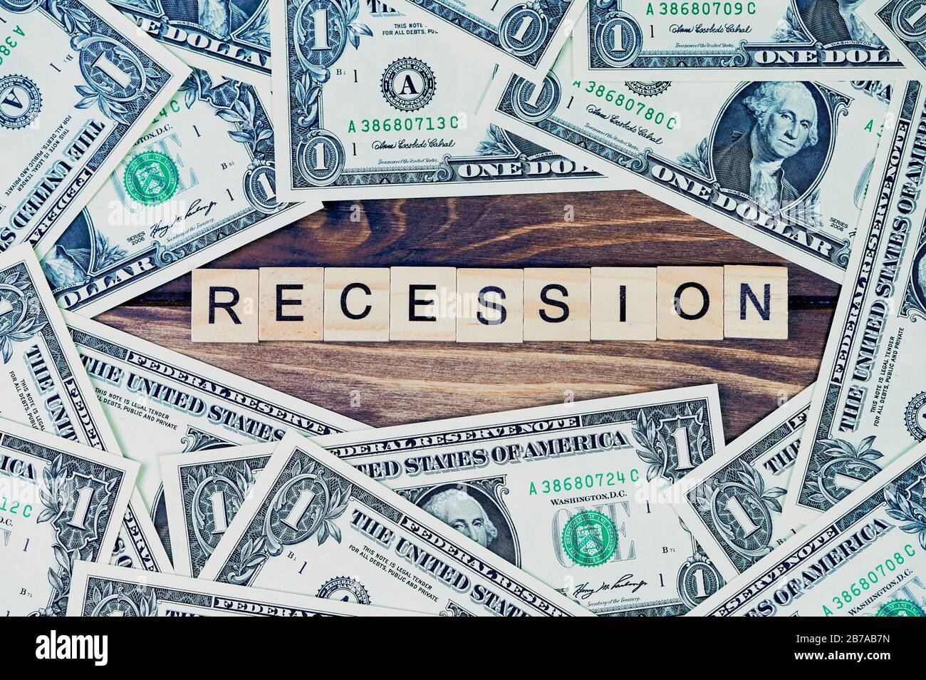Das Wort Rezession in der Mitte auf Holzhintergrund, herum liegen eine Dollarrechnung Stockfoto
