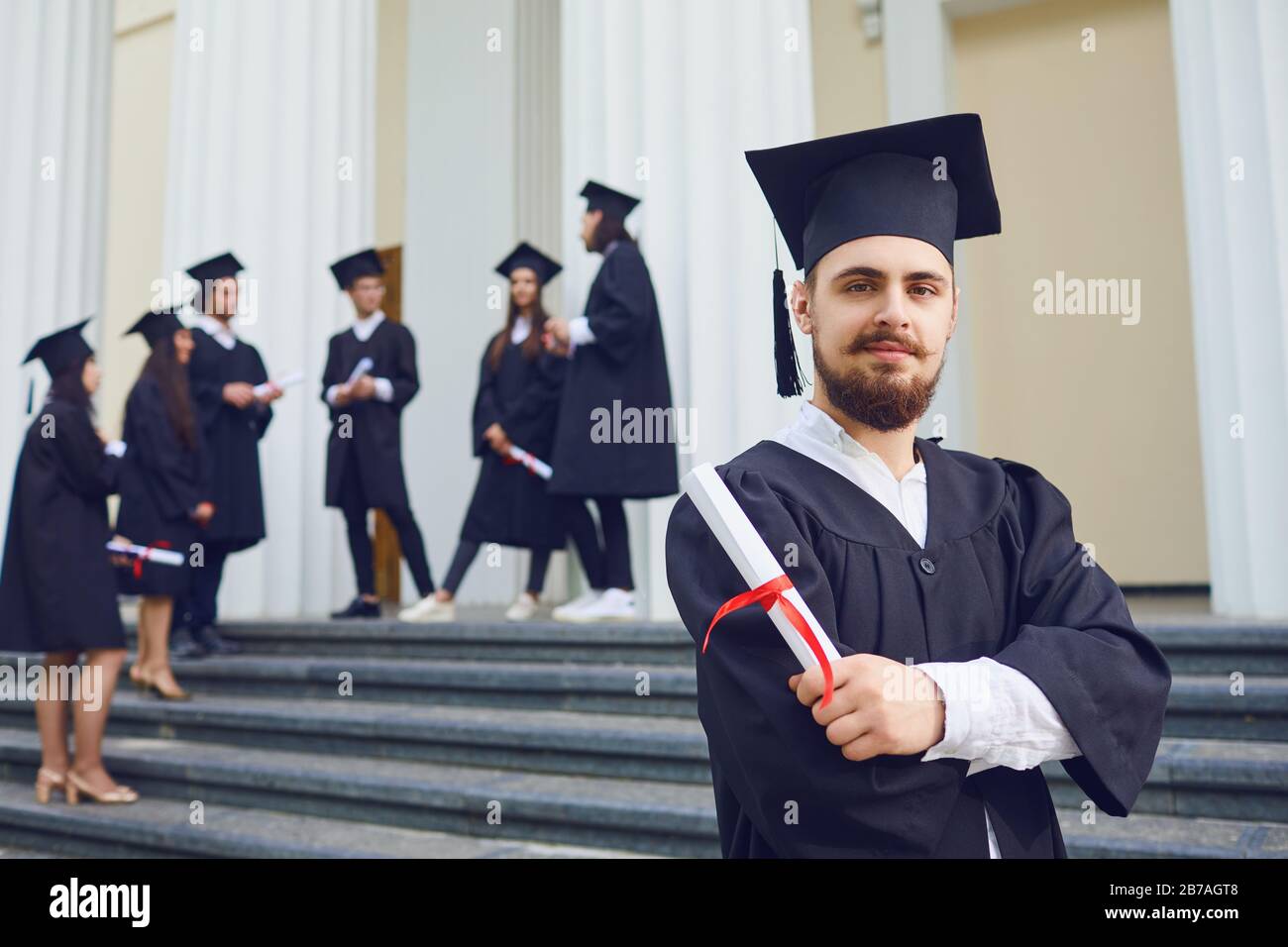 Ein junger männlicher Absolvent vor dem Hintergrund von Hochschulabsolventen. Stockfoto