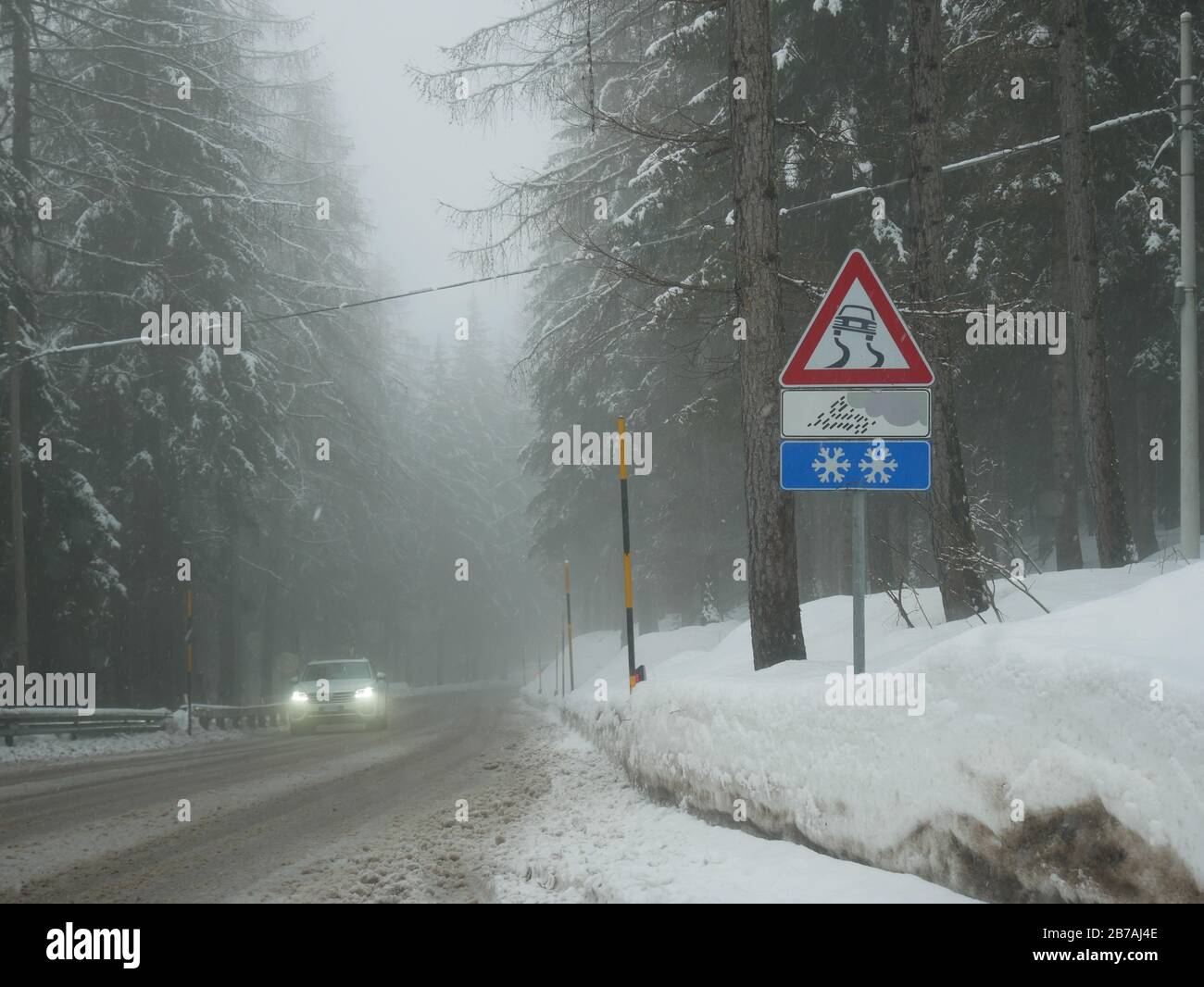 Foggy Day auf den straßen der italienischen alpen und eisiges Straßenschild und ein Auto im Hintergrund Stockfoto