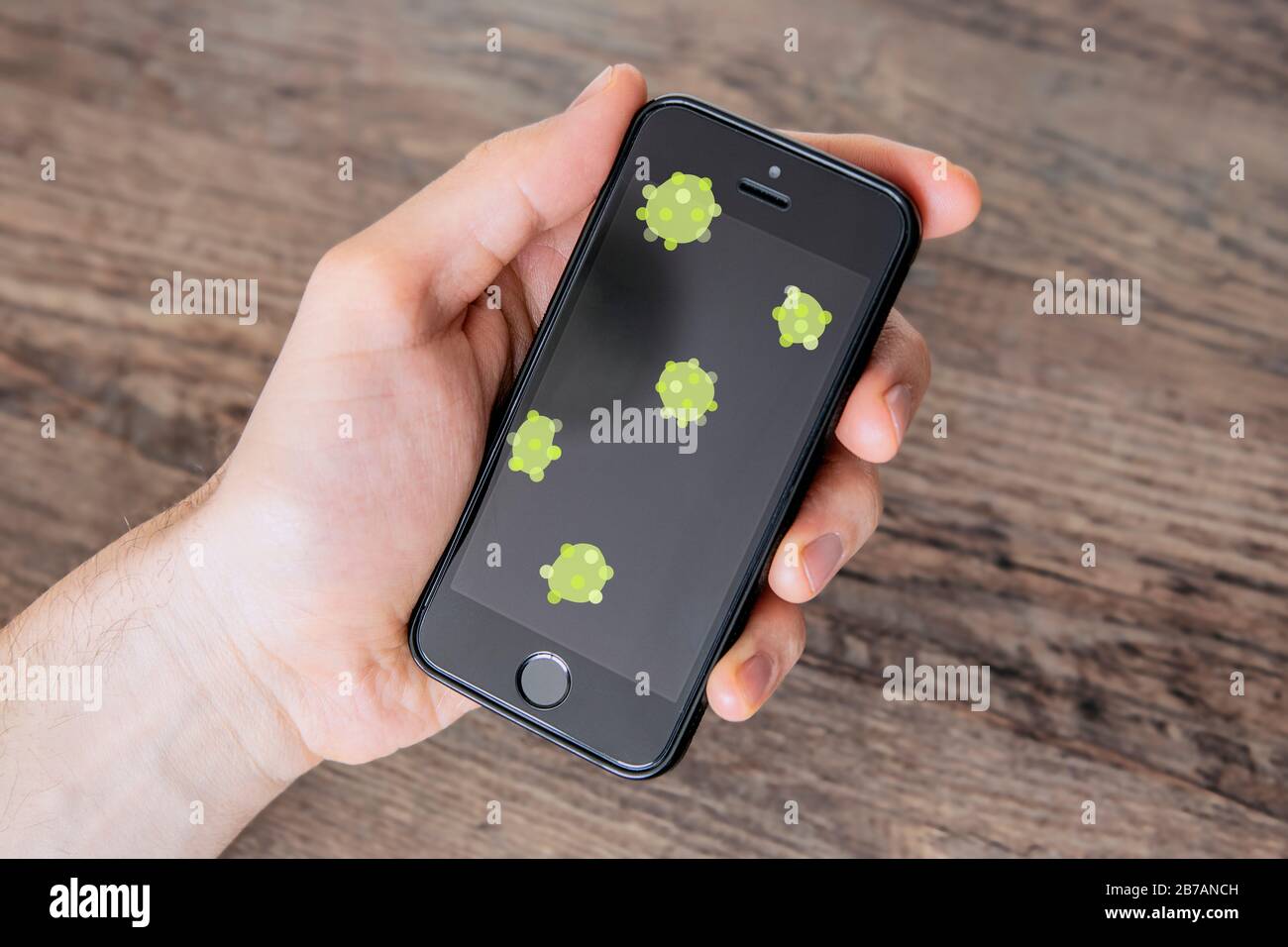 Coronavirus-Zellen auf dem Display des Telefons, linke menschliche Hand. Virusverbreitung durch kontaminierte Oberfläche. Gefahr einer Virusinfektion, Konzept zur Vorbeugung von Coronavirus. Stockfoto