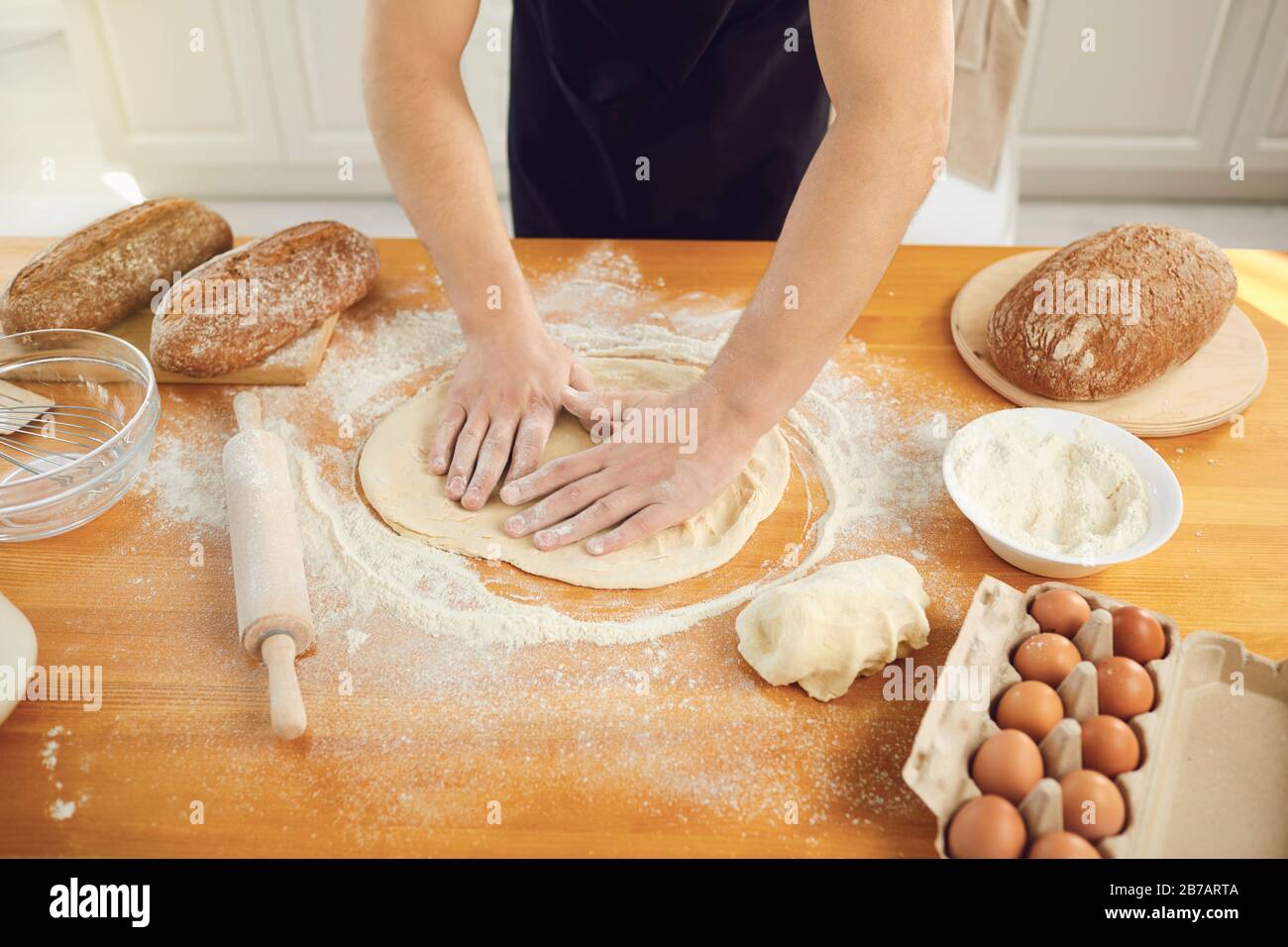 Bärtiger bärtiger Baker-Mann macht frischen Brotteig an einem Tisch in der Backküche. Stockfoto