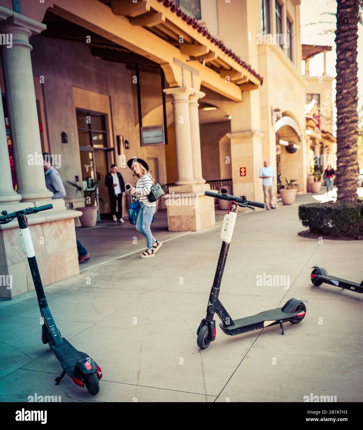 Elektro-Roller werden auf dem Bürgersteig mit Menschen in der Gegend der Scottsdale Waterfront mit Eigentumswohnungen, Restaurants und Einkaufsmöglichkeiten, AZ, planlos geparkt Stockfoto