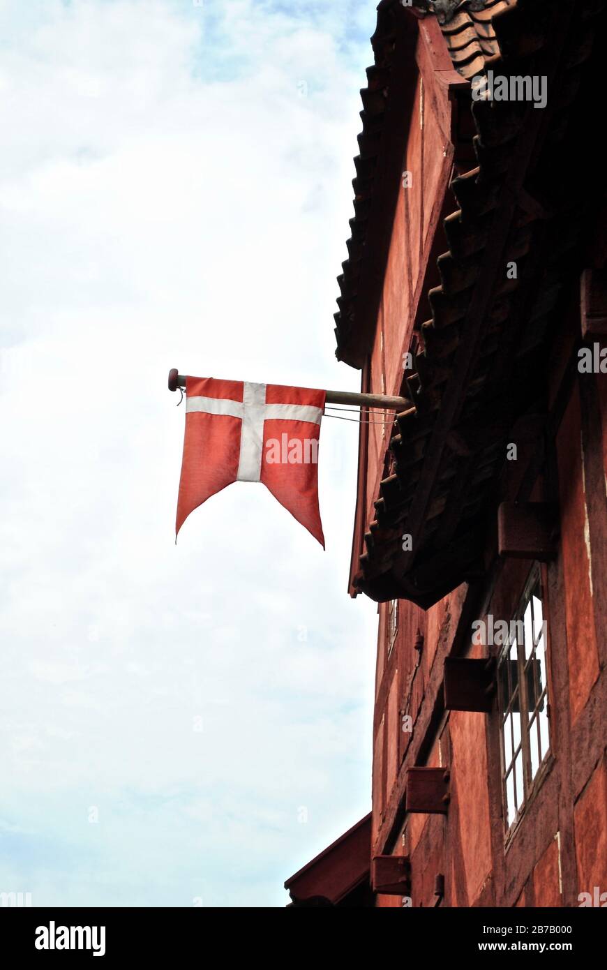 Dänische Flagge hängt von einem roten Haus in den Gamle By (die Altstadt), einem Freilichtmuseum im Botanischen Garten Aarhus, Aarhus, Dänemark. Stockfoto