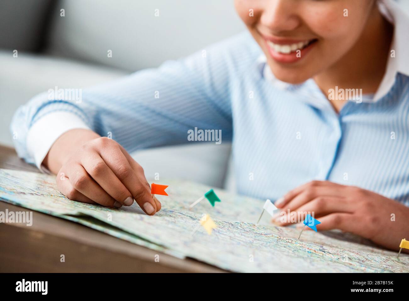 Afrikanische Touragentin mit weiblicher Abstammung sitzt am Tisch im Büro und hält Flaggen auf der Karte und markiert Orte mit fröhlicher Nahaufnahme Stockfoto