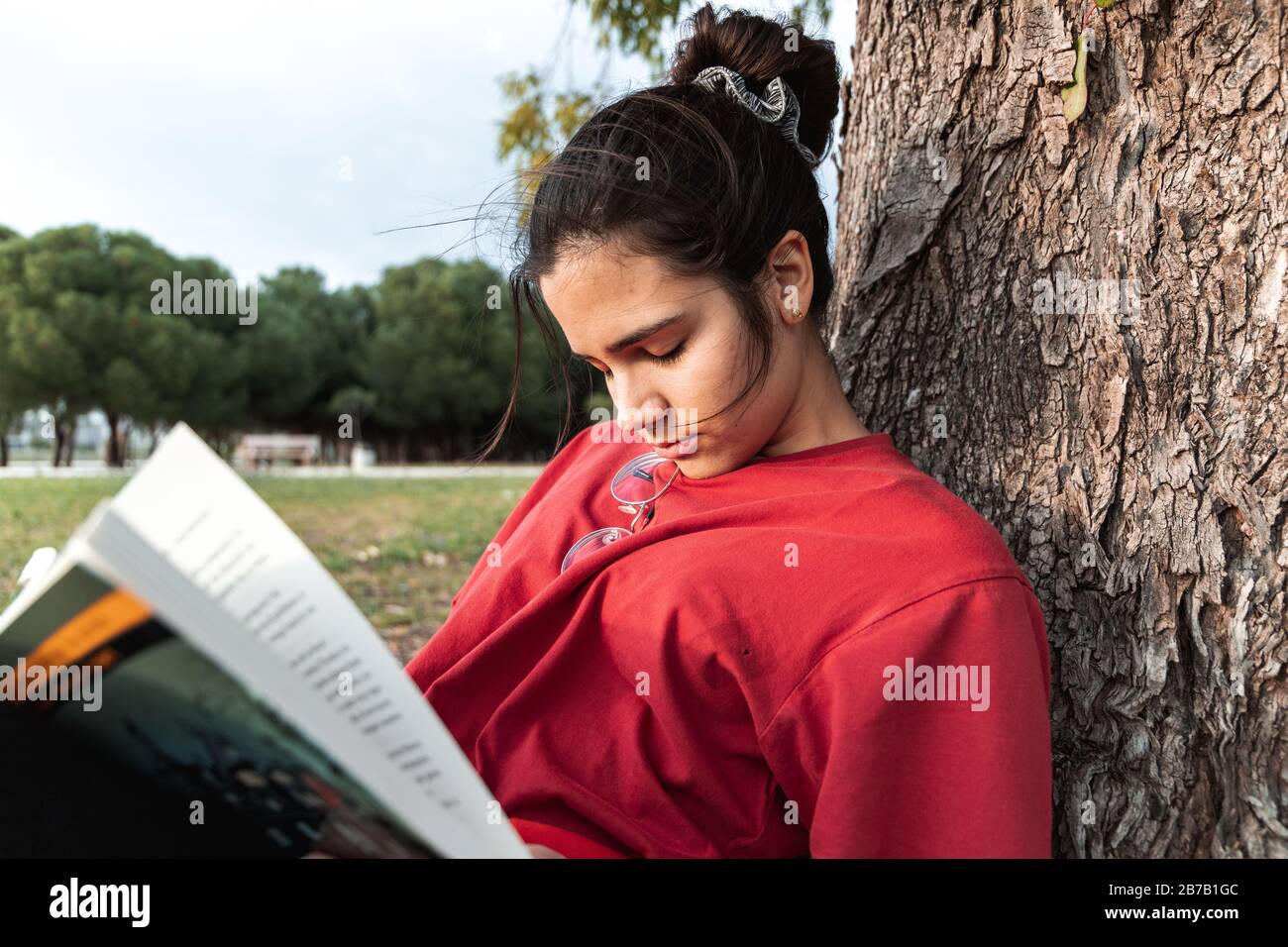 Junge Frau schläft beim Lesen eines Buches und langweilt sich. Sie trägt ein rotes Hemd und hat ihre Brille im Nacken. Sie schläft mit dem Rücken Stockfoto