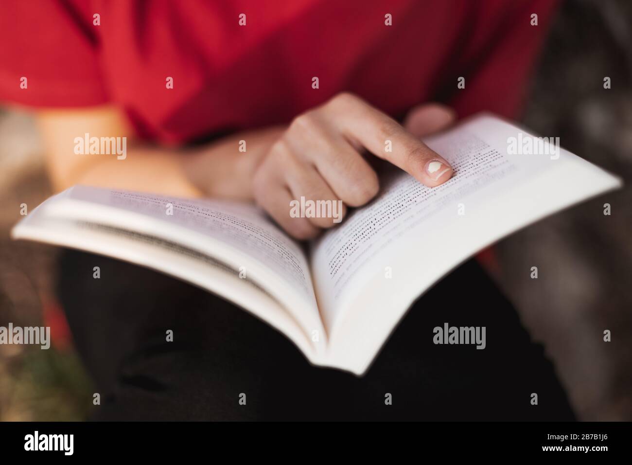 Nahaufnahme eines offenen Buches direkt in der Mitte von einer jungen Frau, die mit dem Finger in ein Wort der Seite zeigt. Geringe Schärfentiefe. Stockfoto