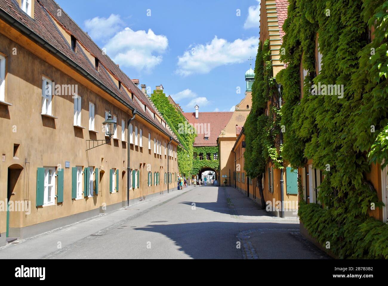 Augsburg: Senfgelbe Wände und grüne verschlafene Fenster der Fuggerei. Die Fuggerei ist der älteste soziale Wohnkomplex der Welt. Stockfoto