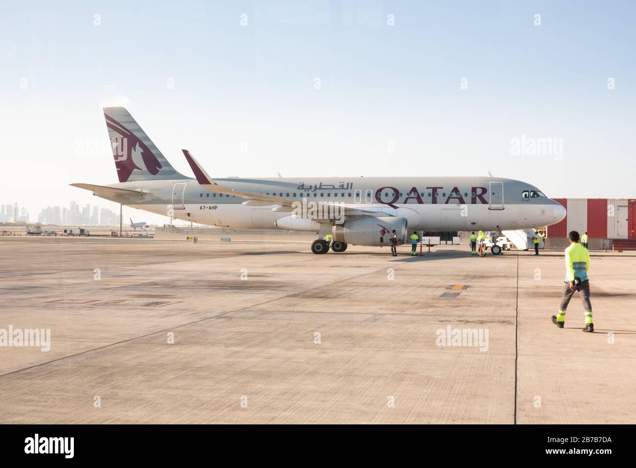 Bodenbesatzungen nehmen an einem Airbus A320 der Qatar Airways, wie er auf einem abgelegenen Stand am Hamad International Airport in Doha parkt, an Stockfoto